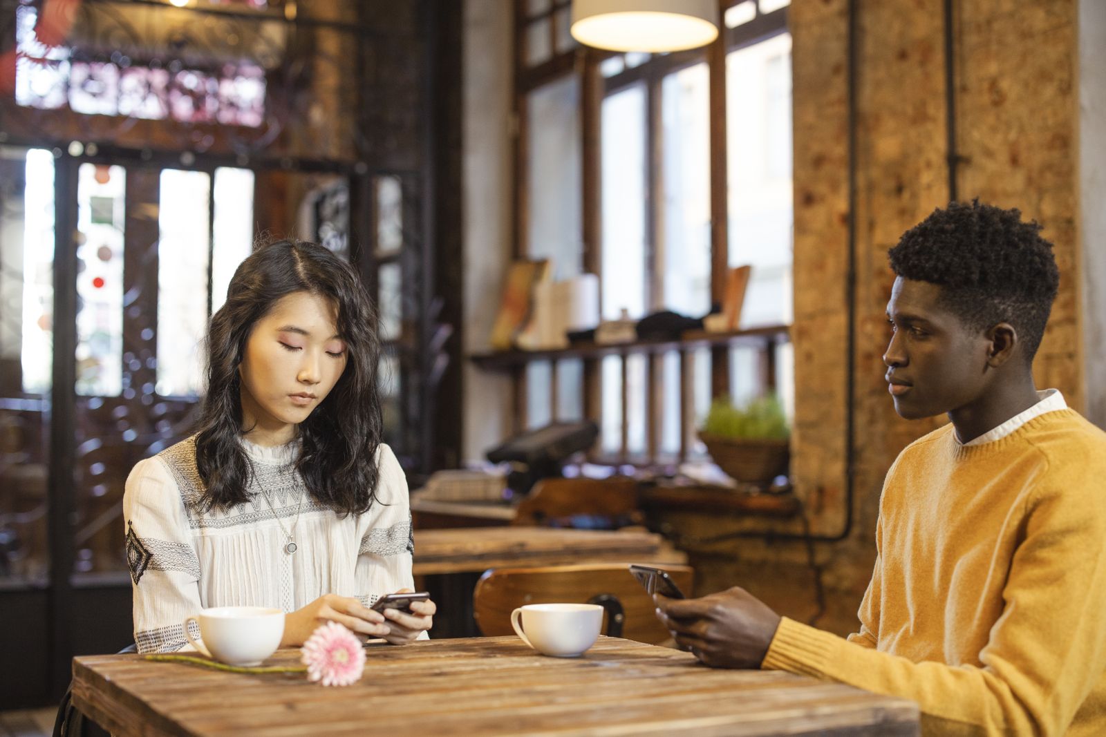 Two young adults sitting across from each other at a cafe while holding their phones