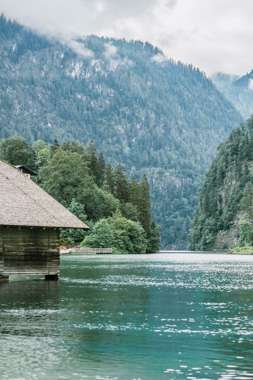Free Relaxing mountain lake view with a wooden cabin and lush trees, perfect for nature lovers. Stock Photo