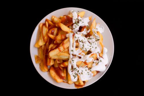 Free A plate of crispy fries topped with creamy sauce and herbs, perfect as a delicious snack. Stock Photo