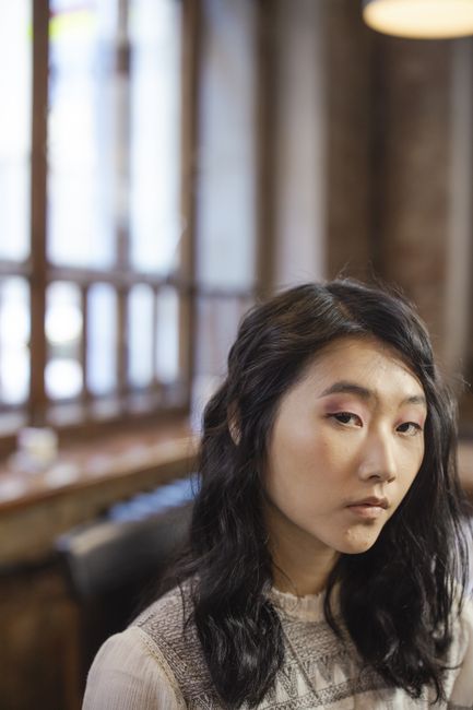 Thoughtful portrait of a woman with black hair, captured in a softly lit indoor setting.