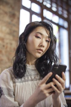 Young woman engaging with her smartphone indoors, capturing a moment of digital interaction.