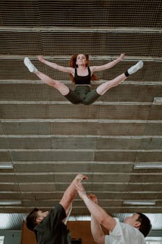 Cheerleaders executing a complex stunt in a gym setting, showcasing teamwork and agility.