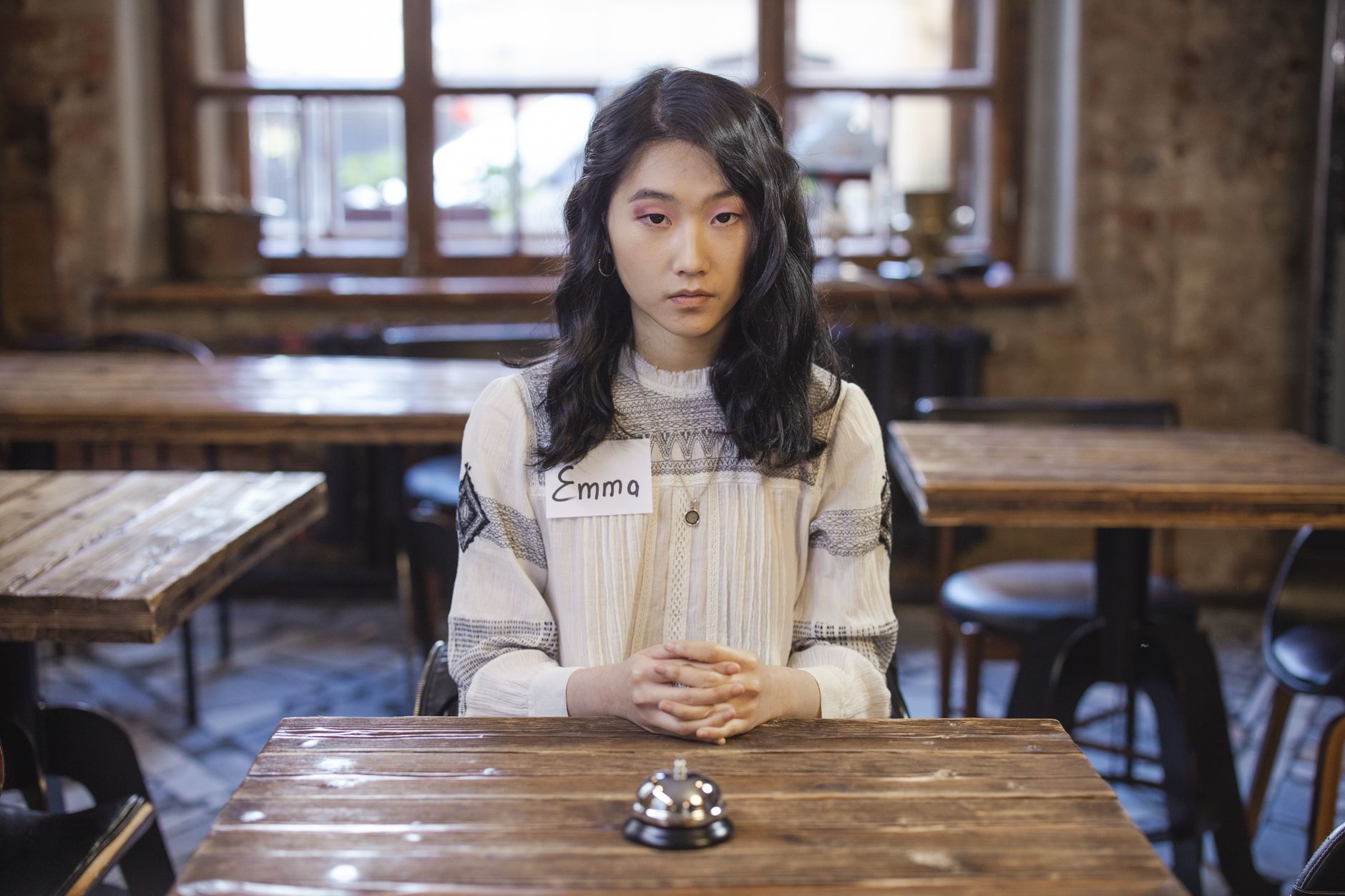 Une femme avec un badge est assise à une table avec une cloche d'appel dans un café rustique.