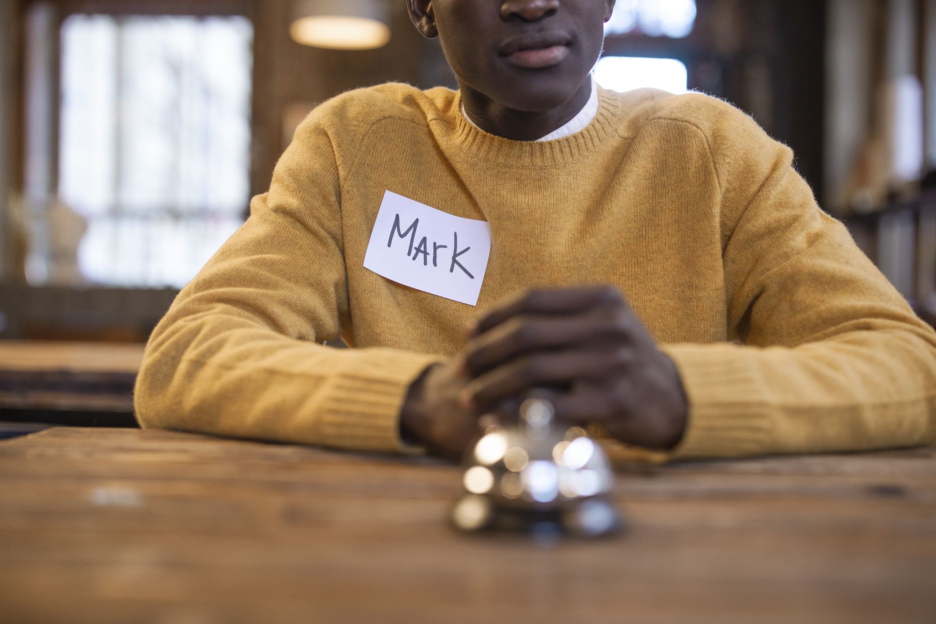 Individual with name tag sitting indoors, suggesting a formal or social gathering setting.