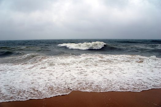 Capture of ocean waves crashing onto a sandy shore under a cloudy sky.