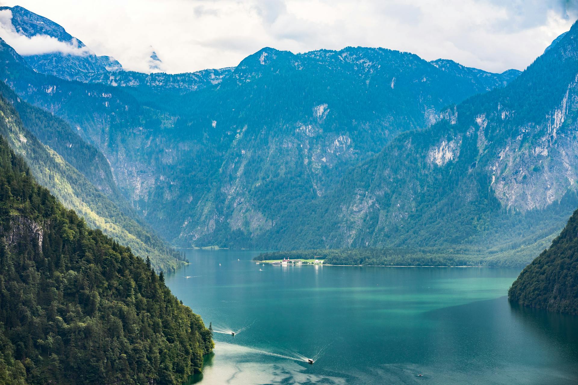 Breathtaking emerald lake surrounded by majestic alpine mountains and lush forests under a cloudy sky.