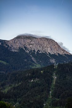 A stunning mountain landscape with cable cars amidst forested slopes at dusk.