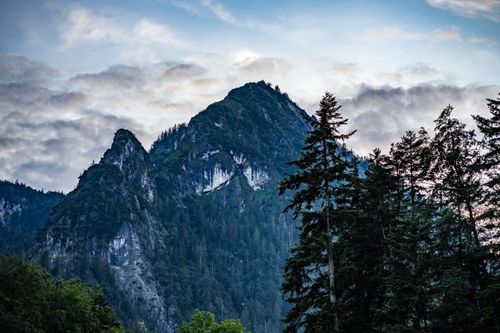 Free Spectacular view of a rugged mountain peak surrounded by evergreen forest under a dynamic cloudscape. Stock Photo