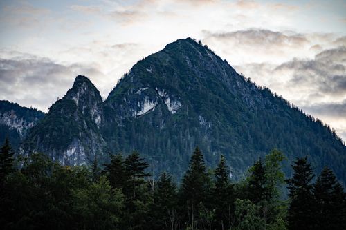 Free Serene view of rocky mountain peaks surrounded by lush forest and dramatic clouds. Stock Photo