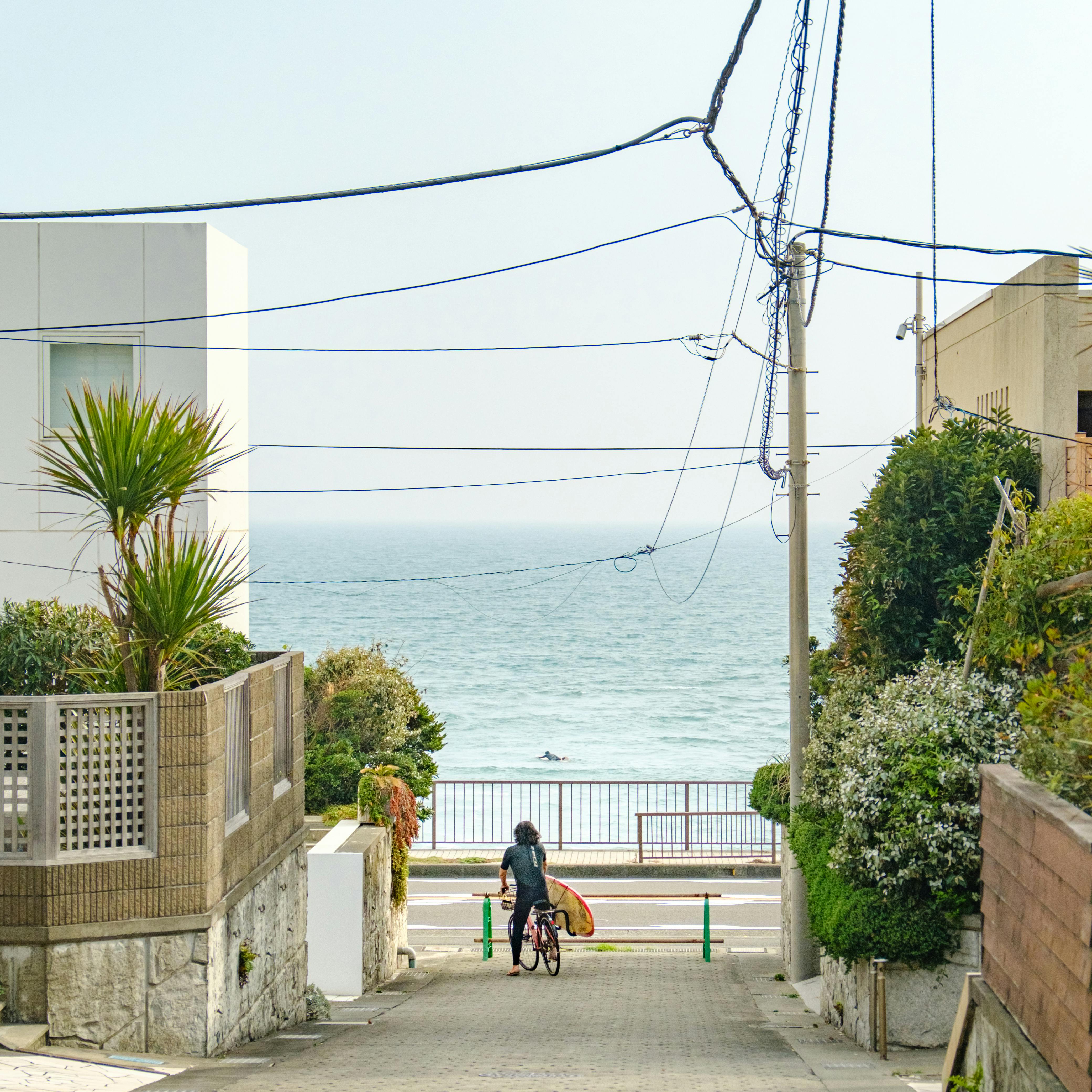 Person biking down a street lined with buildings towards a serene ocean view.