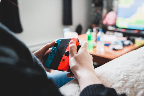 Crop unrecognizable person using console in hands while playing videogame on blurred background