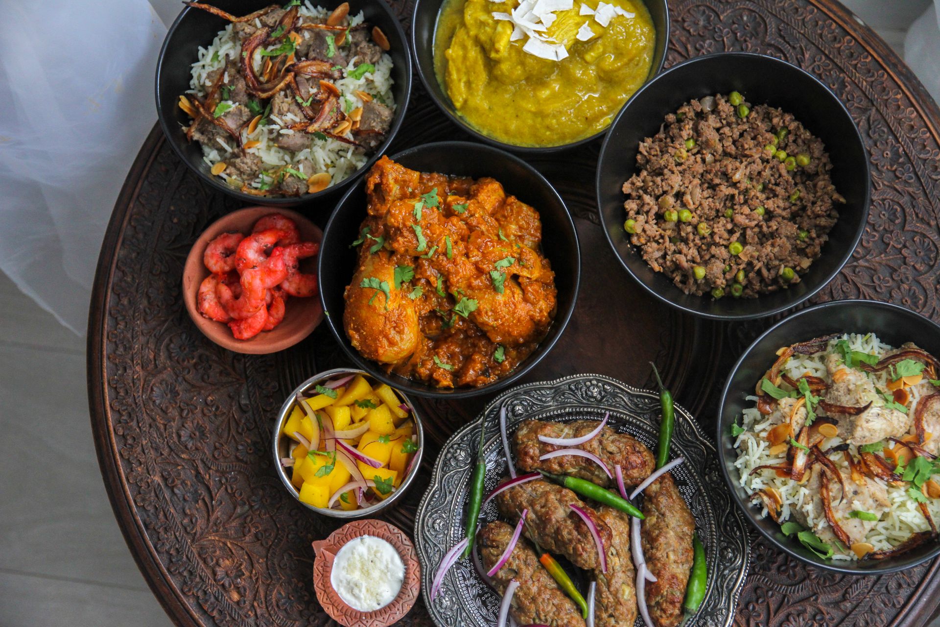 Diverse spread of Indian dishes with curry, meat and sides on a carved table