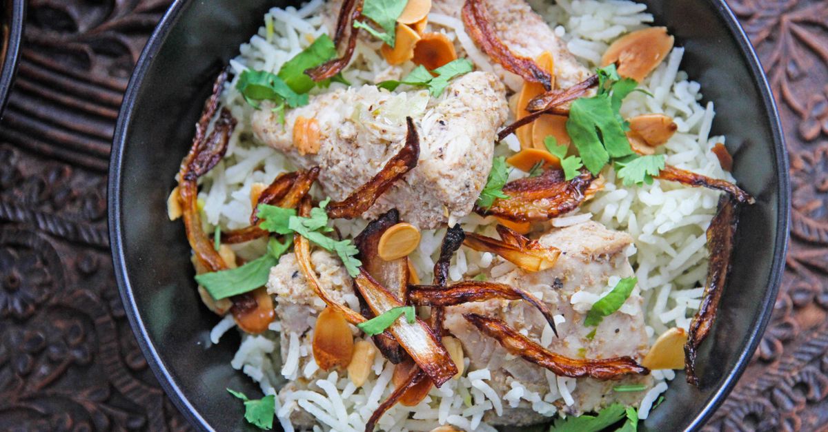 Close-up of traditional Indian chicken biryani garnished with onions and almonds.