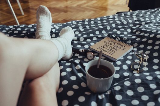 Person relaxing with tea, notebook, and polka dot bedding, creating a cozy atmosphere indoors.
