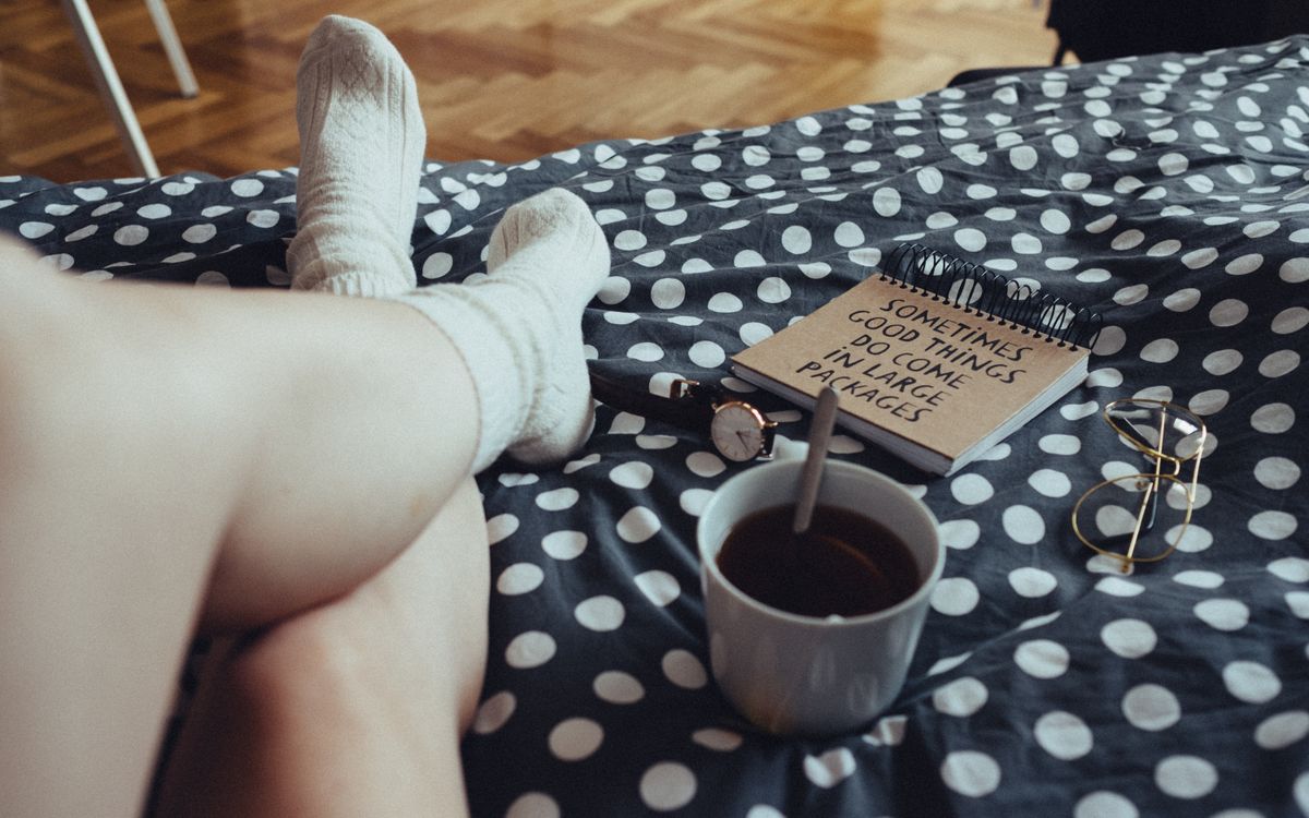 Person relaxing with tea, notebook, and polka dot bedding, creating a cozy atmosphere indoors.