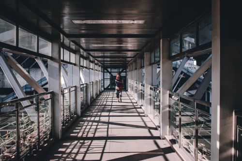 Free A lone woman walks through a steel and glass pedestrian walkway in Makati, Philippines, capturing urban solitude. Stock Photo