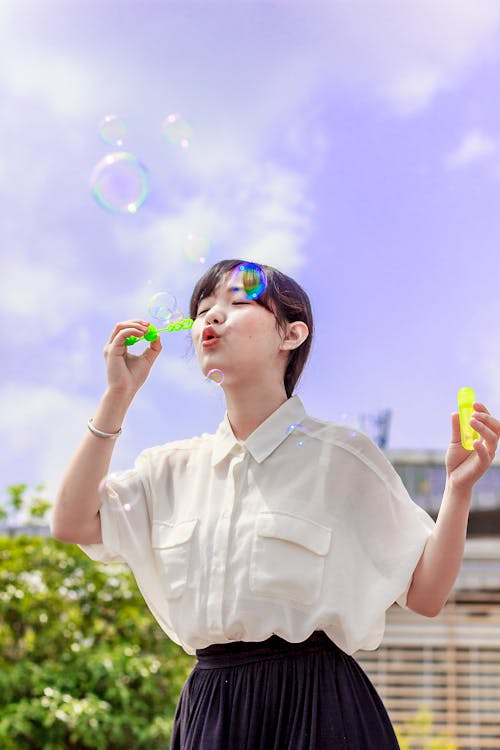 Photo of Woman in White Blouse Playing With Bubbles