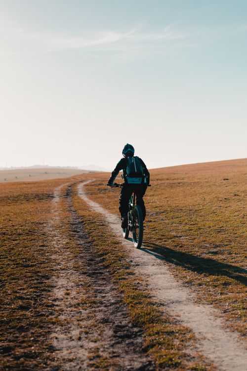 Free Cyclist riding a mountain bike on a winding dirt path through open landscape. Stock Photo