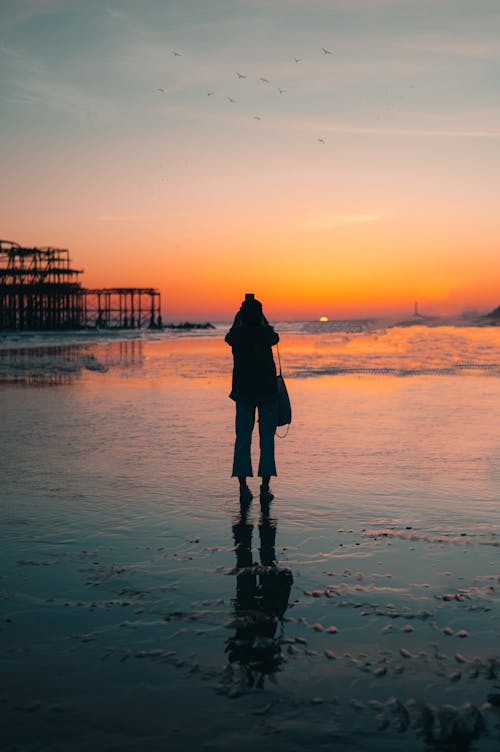 Silhouette of Woman Standing on Beach During Sunset