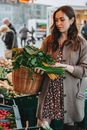 Woman in Gray Coat Holding Brown Woven Basket With Green Vegetable