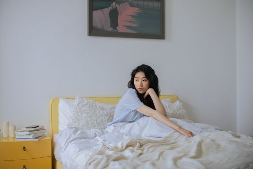 Free Asian woman in a peaceful bedroom, wearing sleepwear, surrounded by cozy decor. Stock Photo