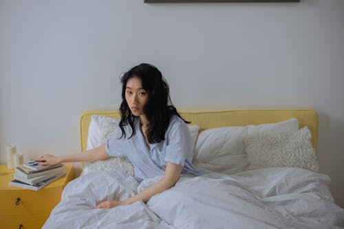 Free Woman Sitting on a Bed With White Linen Stock Photo