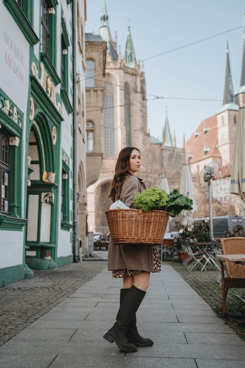 Free Young woman with a basket full of vegetables walking on a charming city street. Stock Photo