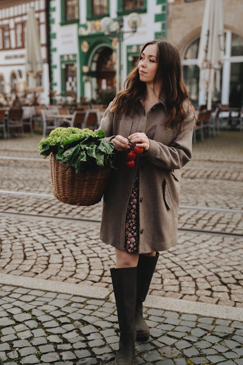 Woman in Brown Coat Carrying Wicker Basket Full of Fresh Vegetables 
