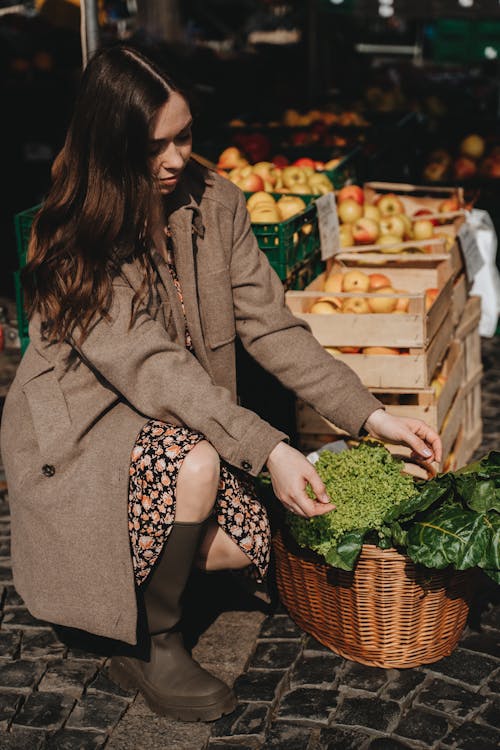 Woman in Brown Coat Holding Green Vegetable in a Basket