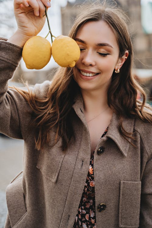 Smiling Woman in Gray Coat Holding Yellow Fruit