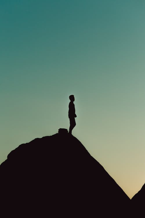 Silhouette of a Man Standing on Top of a Hill at Sunset 