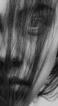 Intimate grayscale close-up portrait of a woman with hair covering her face, creating a conceptual and mysterious mood.