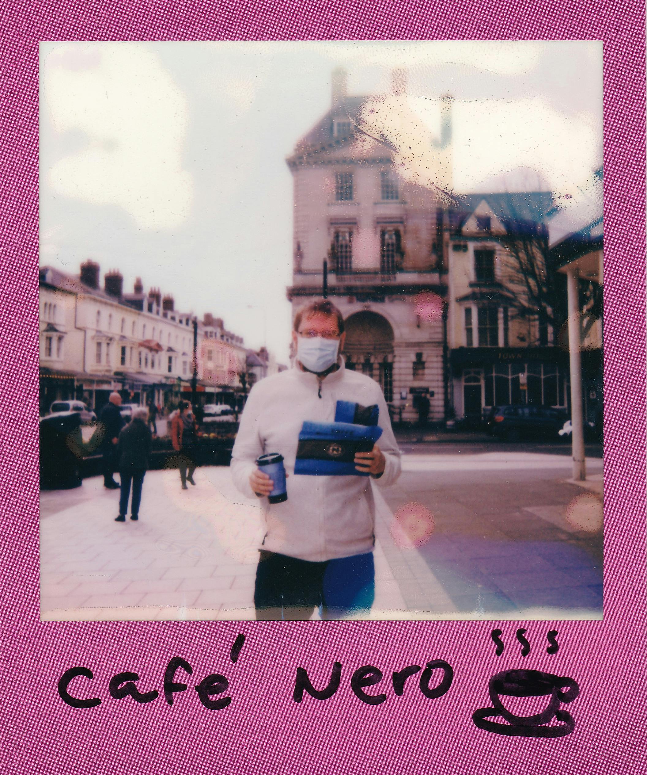 Polaroid photo of a man wearing a face mask holding coffee outdoors in a city.