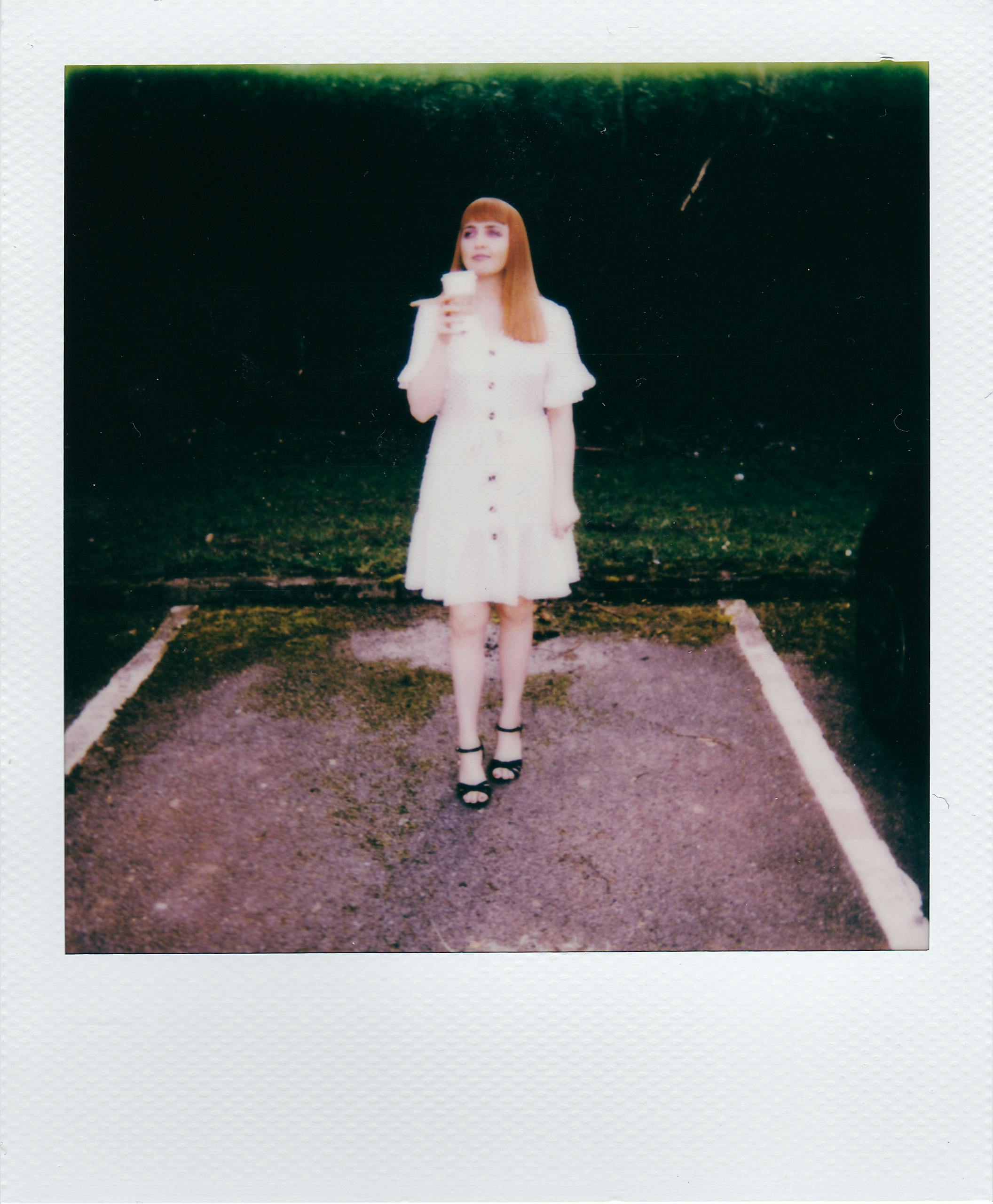 Young woman in a white dress with a cup standing in a parking lot.