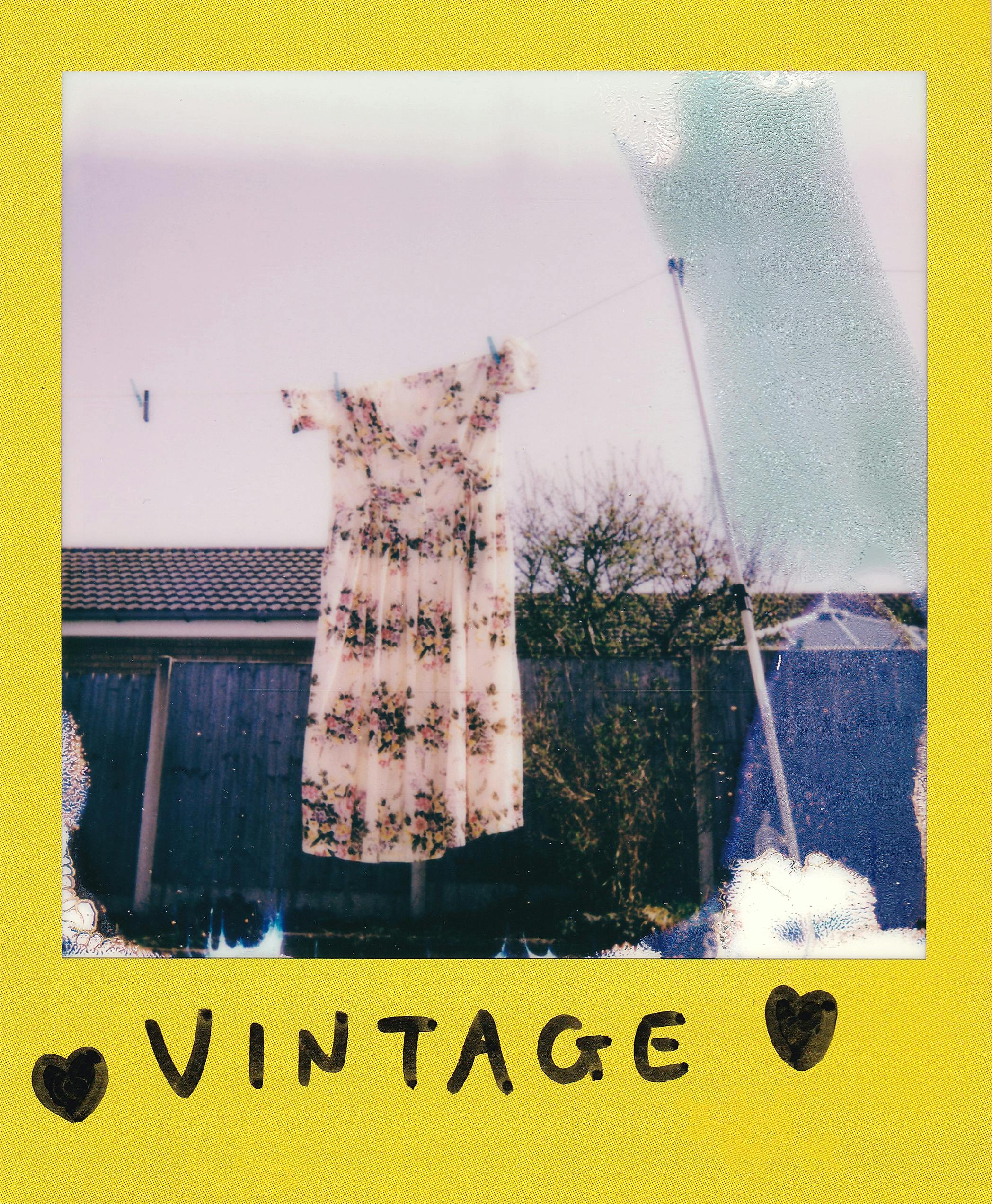A vintage floral dress hangs on a clothesline with a retro Polaroid style.