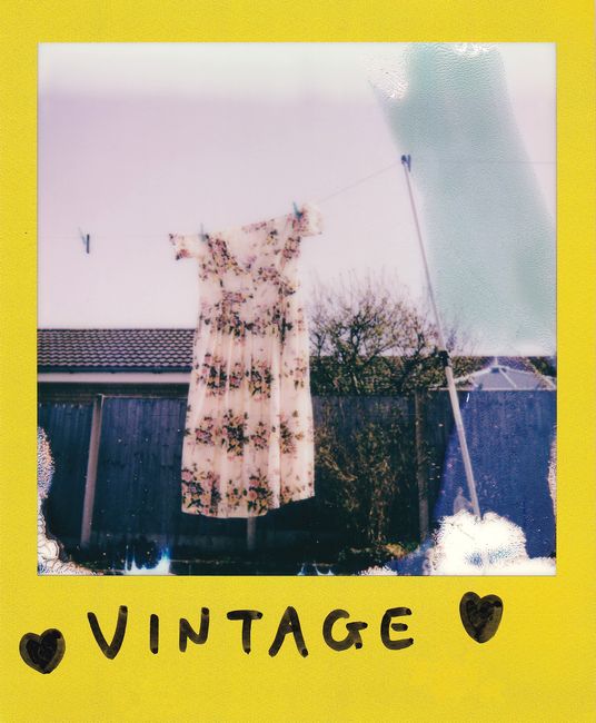 A vintage floral dress hangs on a clothesline with a retro Polaroid style.