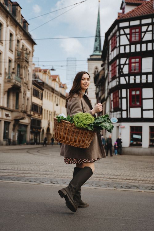 Free Smiling woman carrying greenery in a wicker basket on a vibrant street in Erfurt, Germany. Stock Photo