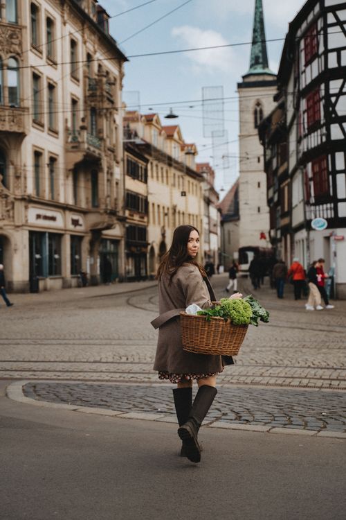 Free A woman with a woven basket shops on a cobblestone street in Erfurt's historic district. Stock Photo