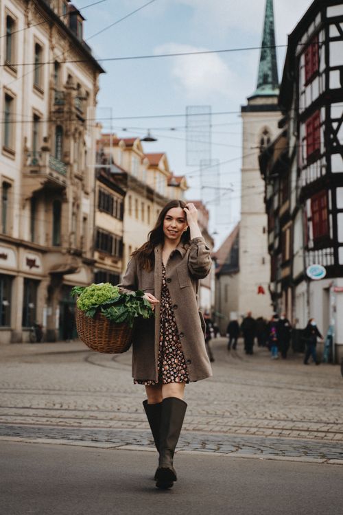 Free Woman in brown coat carrying a wicker basket with greens in Erfurt's historic street. Stock Photo