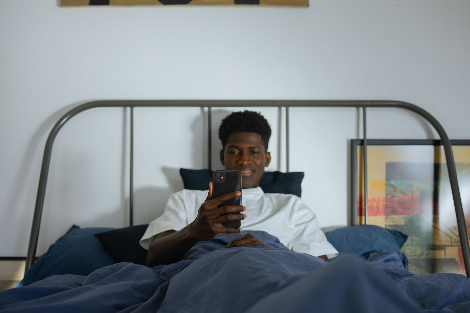 Young man using smartphone in bed, enjoying leisure time at home.