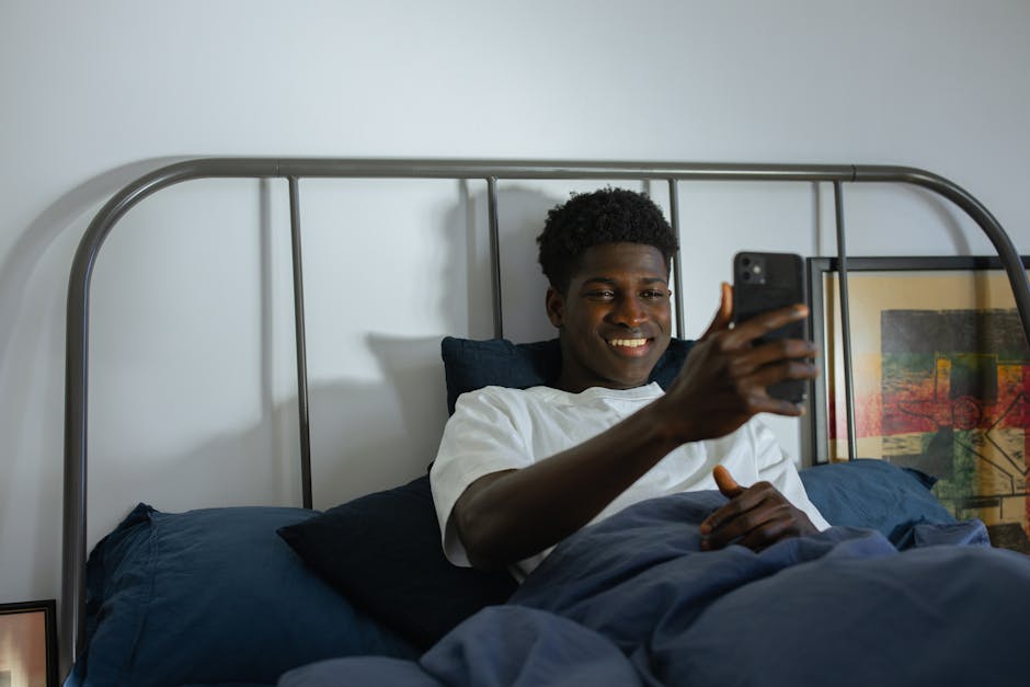 What Sleep Studies Reveal About Adjustable Bed Bases A man smiling while using a smartphone in a modern bedroom setting, illustrating relaxation and connectivity.