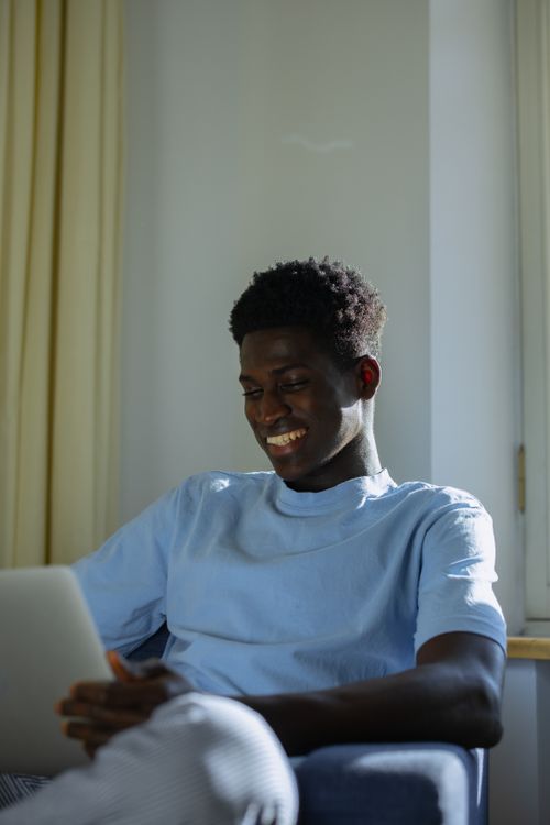 Free Young man smiling while using a gadget at home, enjoying a relaxed moment. Stock Photo