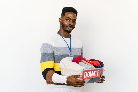 Smiling volunteer holding a donation box filled with clothing against a white background.