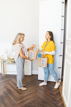 A cheerful woman receives grocery bags from a delivery person at home.