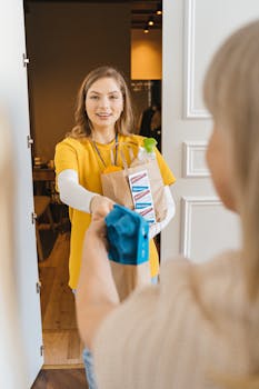 Smiling woman in yellow shirt delivering groceries in paper bag to a senior at the door.