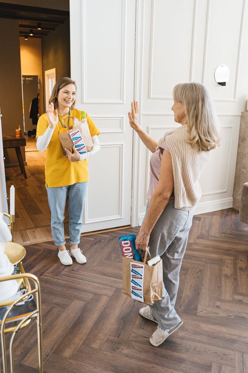 Free A warm interaction indoors with a delivery person and an elderly customer exchanging waves and smiles. Stock Photo