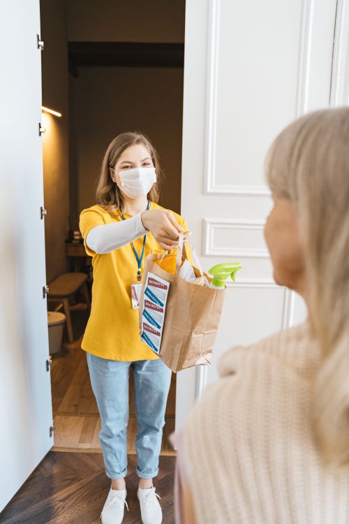Free A volunteer provides groceries to an elderly woman at her doorstep, showcasing community support. Stock Photo