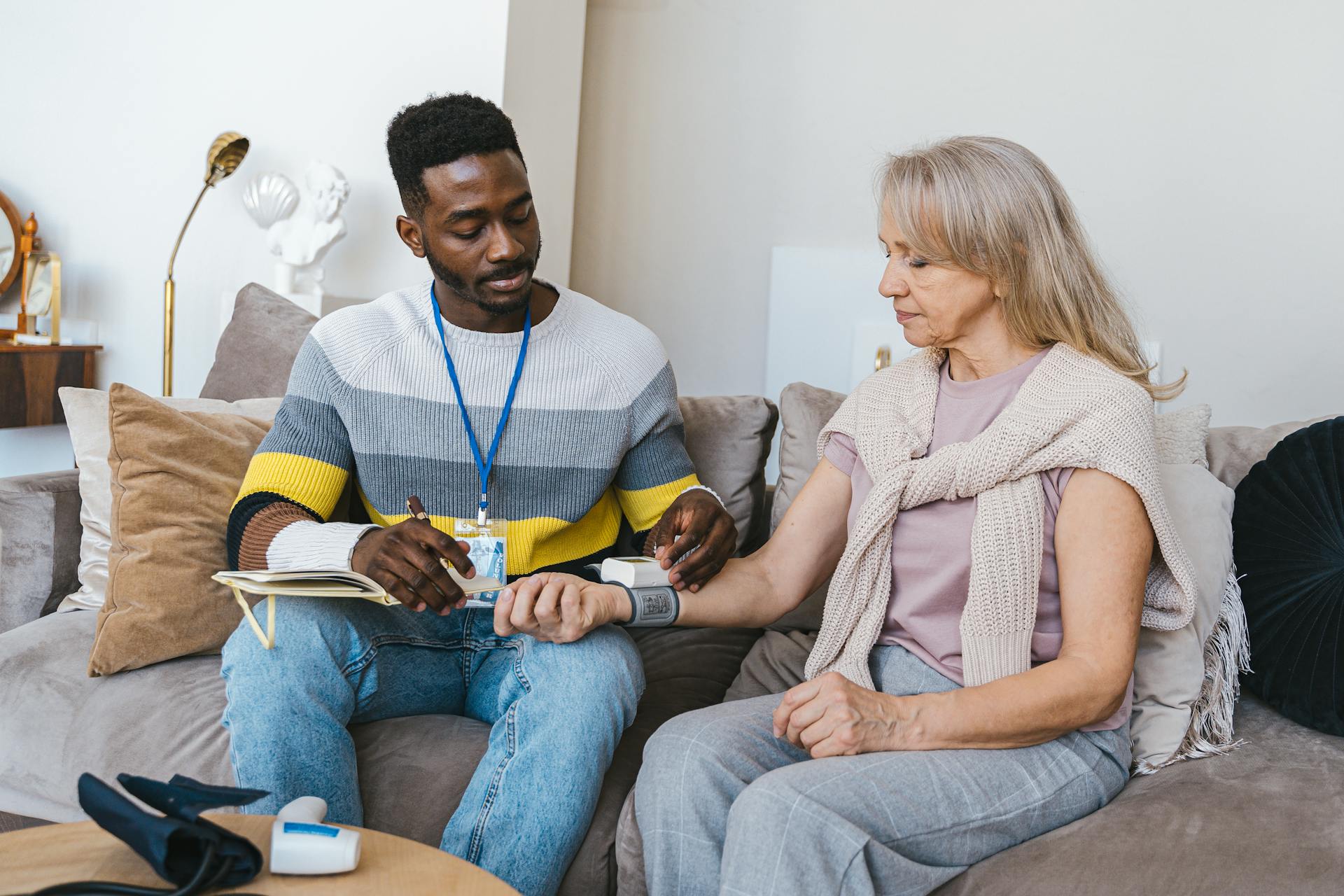 Volunteer checking elderly woman's blood pressure at home. Compassionate healthcare support.