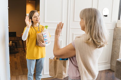 Two Women Carrying Paper Bags Waving