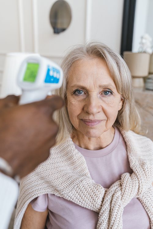 Free Elderly woman smiling while her temperature is checked with a digital thermometer. Stock Photo